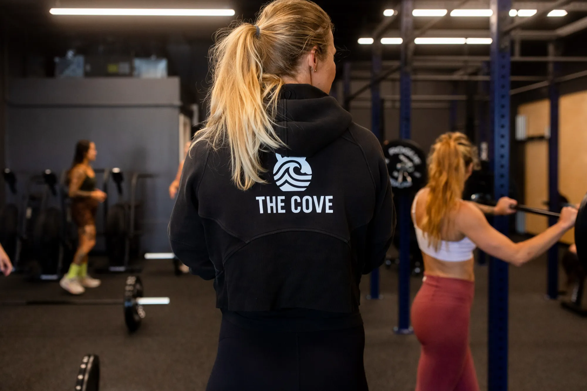 A member wearing a black hoodie with The Cove logo on the back, training on the gym floor.